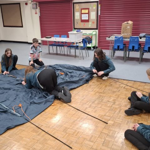 A team of Scouts working together to thread poles through the sleeves of a new tent